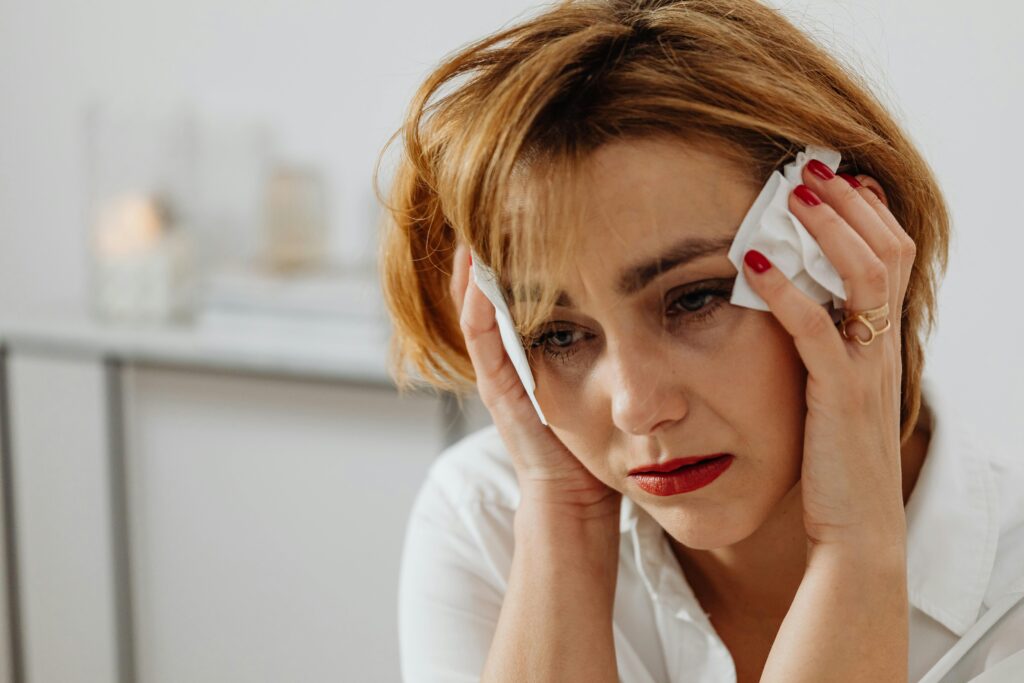 pexels-photo-6028541-6028541 Close-up of a woman in distress holding tissues, expressing emotional sadness.